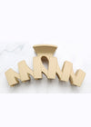 Beige hair clip with 'MOM' letters on a white marble background