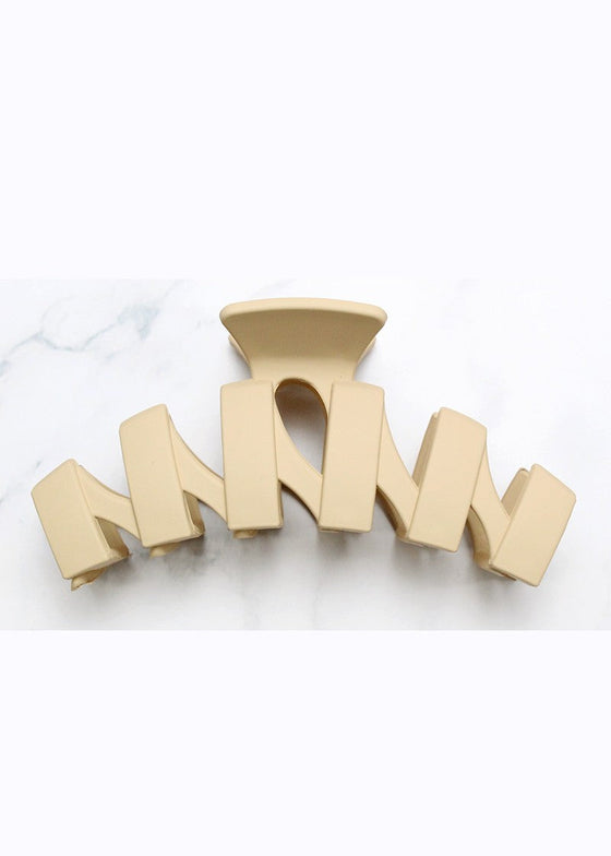 Beige hair clip with 'MOM' letters on a white marble background
