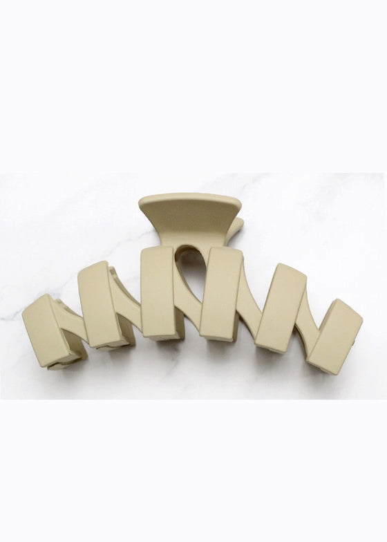 Beige hair clip with 'M' design on a white background