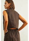 Woman wearing a brown sleeveless top and pants against a white background