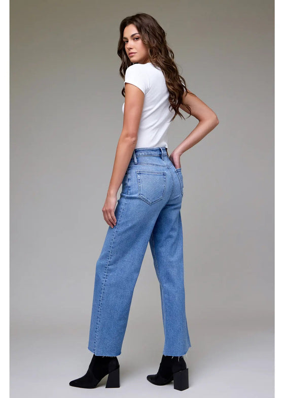 Woman wearing blue jeans and a white top on a plain background