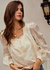 Woman wearing a white lace blouse with long sleeves against a neutral background
