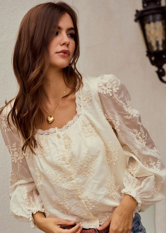 Woman wearing a white lace blouse with long sleeves against a neutral background