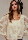 Woman wearing a white lace blouse with sheer sleeves against a neutral background
