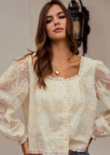  Woman wearing a white lace blouse with sheer sleeves against a neutral background