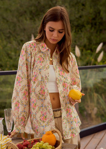  Woman in a floral shirt holding a lemon outdoors with a basket of fruits on a table.