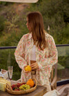 Woman in a floral kimono standing by a table with a fruit basket outdoors.
