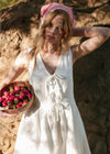 Woman in a white dress holding a basket of flowers against a stone wall.