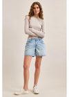 Woman wearing a light gray long-sleeve top and denim shorts on a plain background