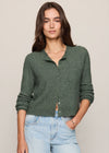 A woman modeling a dark green cable-knit button-up cardigan sweater paired with light-wash blue jeans, set against a plain beige studio background.