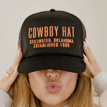  Black cap with orange text worn by a person, against a neutral background