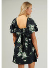 Woman wearing a black floral dress with puff sleeves on a plain background