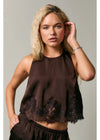 A blonde model wearing a dark brown satin sleeveless top with a black lace hem, paired with matching dark brown bottoms, against a neutral gray studio background.