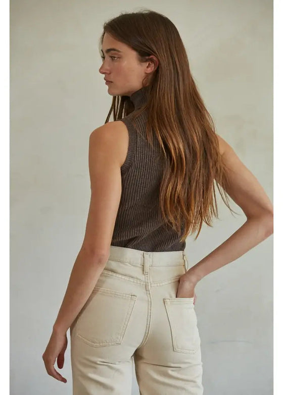 Woman wearing a brown ribbed tank top and beige pants against a neutral background