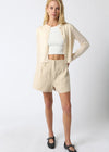 Woman wearing a beige cardigan, white top, and shorts on a white background