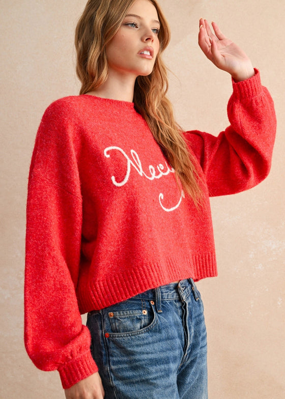 Person wearing a red sweater with 'Please' text and blue jeans against a beige background