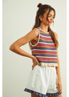 Woman wearing a colorful striped sleeveless top and white shorts on a light background