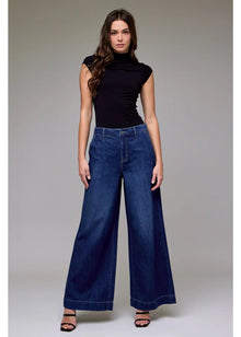  Woman wearing a black top and blue wide-leg jeans on a gray background