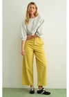 Woman wearing a light gray cropped sweater and yellow pants against a white background