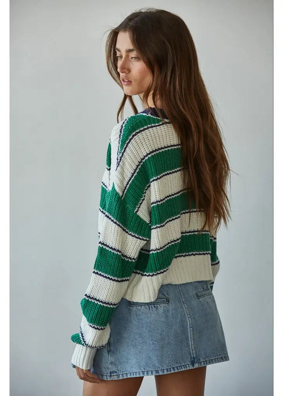 Woman wearing a green and white striped sweater with a denim skirt against a plain background