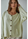 Woman wearing a light green cardigan with buttons against a plain background