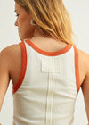Person wearing a white tank top with orange trim on a plain background