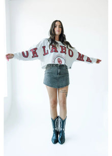  Person wearing a white sweatshirt with red text, denim skirt, and cowboy boots on a white background