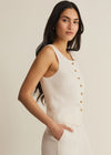 Woman wearing a white sleeveless top with gold buttons on a beige background