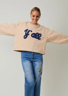  Person wearing a beige sweatshirt with 'Y'all' text and blue jeans on a plain background