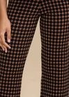 Close-up of a person wearing brown wide-leg pants with a black polka dot pattern, showing the hands and legs against a plain beige background.