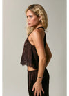 A woman in side profile wearing a dark brown sleeveless top with lace trim and matching dark brown pants, photographed against a plain light gray studio background.