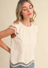 Woman wearing a cream-colored top with lace details on a beige background