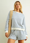 Woman wearing a blue and white striped outfit with a beige bag against a plain background