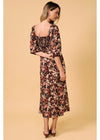 A woman modeling a floral midi dress from the back, featuring a square open back, elbow-length sleeves, and a smocked bodice, set against a solid beige background.
