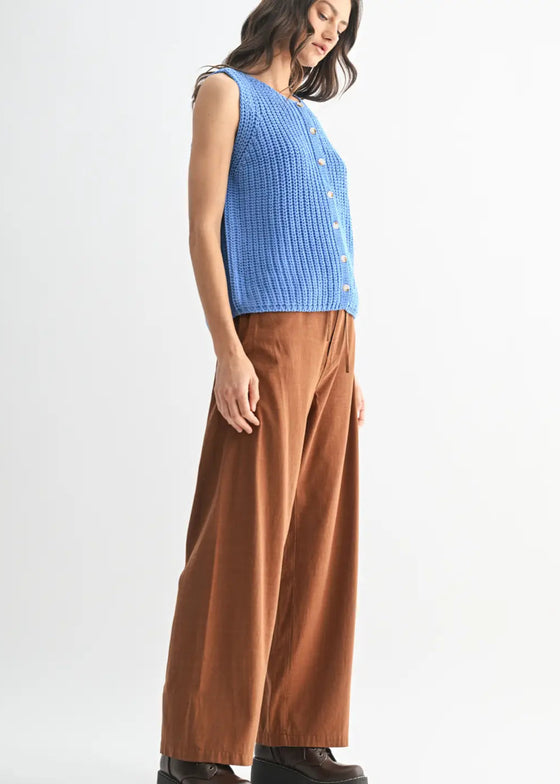 Person wearing a blue sleeveless top and brown pants on a white background