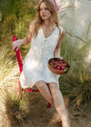 Woman in a white dress sitting on a red chair holding a basket of fruit in a natural setting.