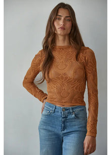  Woman wearing a brown lace top and blue jeans against a plain background