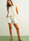 Woman wearing a white romper with lace details on a plain background