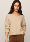 Woman wearing a beige sweater and brown pants against a plain background