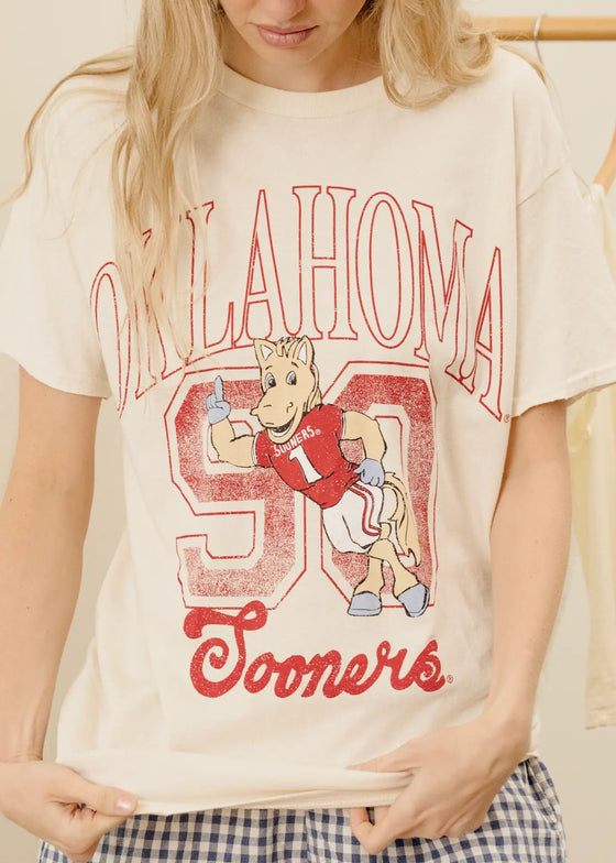 Person wearing a 'Oklahoma Sooners' t-shirt with a cartoon character on a beige background