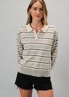 A woman modeling a light gray and cream striped knit polo sweater with black horizontal stripes, paired with black denim shorts, against a solid gray studio background.