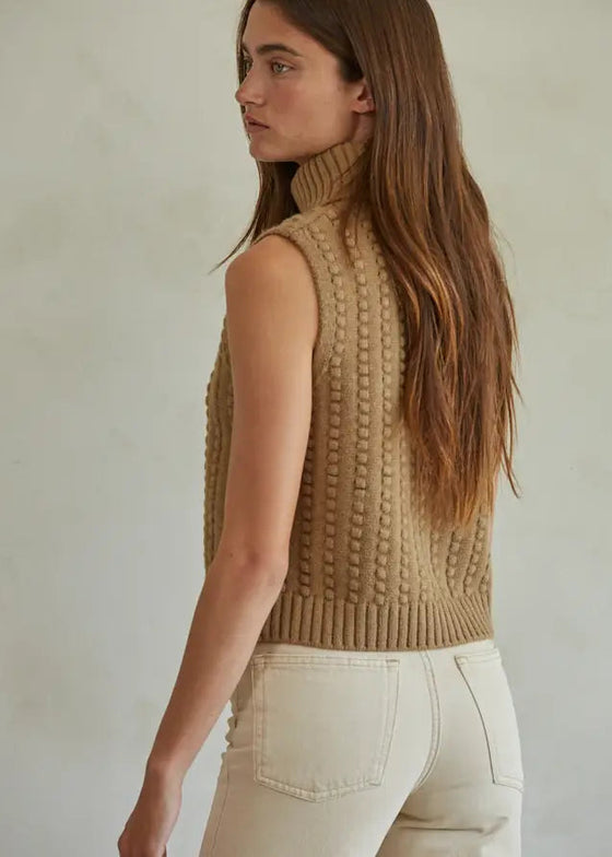 Woman wearing a beige knitted vest against a plain background
