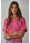 Woman wearing a pink knitted sweater against a gray background