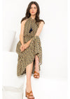 A woman models a sleeveless high-low midi dress with a yellow and black abstract pattern, sitting on a white bench against a white background.