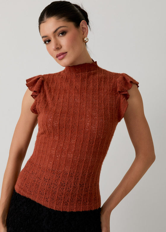 Woman wearing a rust-colored ribbed top with ruffled shoulders against a plain background