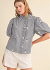 Woman wearing a blue and white striped blouse with floral embroidery on a beige background