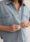 Person wearing a light blue denim shirt with a neutral background