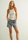 Woman wearing a white tank top with red trim and denim shorts on a plain background