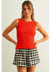 Woman wearing a red sleeveless top and plaid skirt on a plain background
