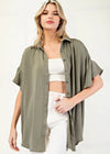 Woman wearing an olive green shirt over a white top and pants on a white background